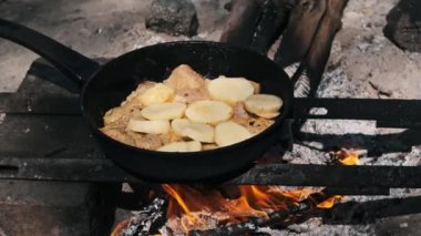 Kamp ateşinde tavada kızartılmış patatesli tavuk. Otantik açık hava pişirme deneyimi.