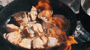 Kamp ateşinin üstünde tavada cızırdayan tavuk ve soğan yakın çekim. Et mükemmel pişiyor, basit ama lezzetli bir açık hava yemek deneyimi sergiliyor..