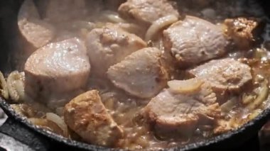 Kamp ateşinin üstünde tavuğun parçaları ve soğan cızırtılarının yakın plan görüntüsü. Lezzetli et ve karamelli soğan kırsal bir açık hava yemeğinin çekici bir görüntüsünü oluşturur..