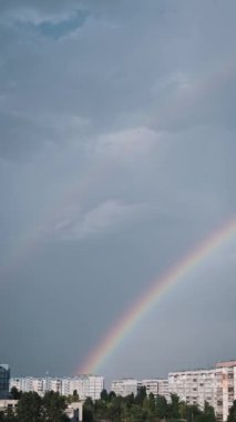 Çarpıcı dikey görüntüler, canlı bir gökkuşağının şehir manzarası üzerinde yayılışını gösteriyor. Bulutlu gökyüzüne karşı renkli bir yay umut verici ve ilham verici bir sahne yaratır..