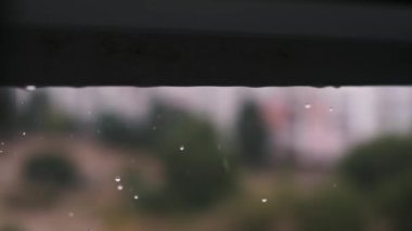 Arka planda bulanık bir şehir manzarası olan pencere pervazından düşen yağmur damlalarının yavaş çekim görüntüleri. Bu sakin sahne, şehir ortamında yağmurlu bir günün güzelliğini yakalar..