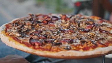 Sosisli, mantarlı ve soğanlı lezzetli bir pizza, ahşap bir stantta servis ediliyor, İtalyan mutfağı ve yemek fotoğrafçılığı için mükemmel..