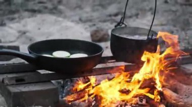 Kaynar suyla siyah kazan ve kabak dilimli kızartma tavası. Kamp ateşinde pişiyor. Basit bir açık hava yemeği hazırlığı..