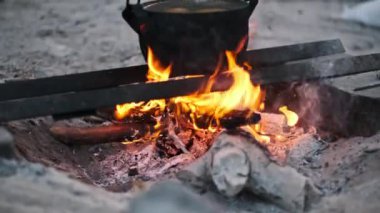 Ateşin sıcaklığını ve enerjisini tasvir etmek için yukarıda kaynayan bir tencere gibi odunları yutan bir kamp ateşinin yakın çekimi..
