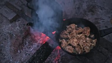 Tavuk parçaları cızırdıyor ve tavada kızaran közlerden oluşan bir yatağın üzerinde pişerken patlıyor. Geleneksel çaydanlık yakınlarda oturur, kamp ateşinin özünü yakalar..