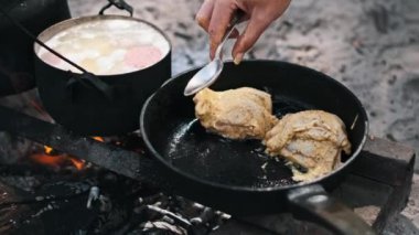 Terbiye edilmiş tavuk butları bir kamp ateşinin üstünde kızartılıyor. Lezzetli bir açık hava pişirme deneyimi..
