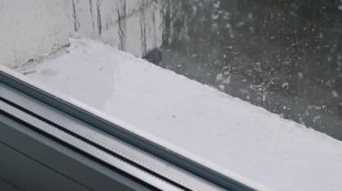 Pencerenin penceresinden süzülen ve pencerenin pervazında toplanan yağmurun yakın çekim görüntüleri dışarıdaki manzarayı bulanıklaştırıyor. Huzurlu ve düşünceli bir ruh hali yaratır..