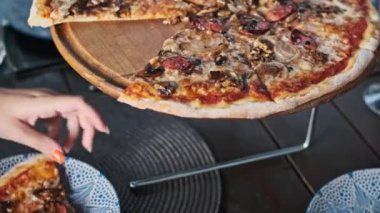 Bir el bir dilim pizzaya uzanır sosis, mantar ve soğanla, ahşap bir stantta servis edilir, yemek paylaşımı ve yemeğin tadını çıkarmak için mükemmeldir..