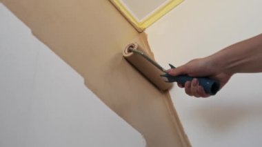Bir kadın duvar bejini boya rulosuyla dikkatlice boyuyor. Düşük açılı bir perspektiften yeni bir kat boya sürüyor..