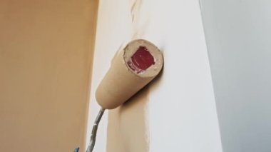 Bir adam odanın köşesini bej renkli bir boya rulosuyla boyuyor. Duvarları yavaş çekimde boyama işlemi, dikey video.