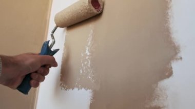 Kısmen boyanmış beyaz bir duvara bej boya sürmek için boya silindiri kullanan insanlar, yenileme işlemini yavaş çekimde gösteriyor..