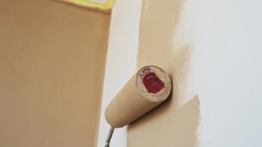 Beyaz bir duvara bej boya sürerek düz olmayan bir yüzey oluşturan bir boya silindiri yakın plan..