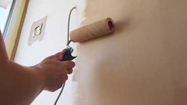 Bir kadın boya rulosu kullanarak beyaz bir duvar bejini boyuyor. Kamera açısı aşağıdan, bu işlem için eşsiz bir bakış açısı sağlıyor..