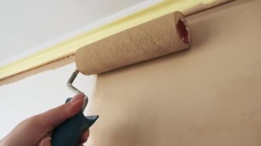 Bir kadın beyaz bir duvar bejini rulo ile boyuyor. Sarı tavan kalıbı yukarıdan görülebiliyor. Tamir, yenileme ve ev geliştirme konsepti.