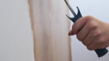 Beyaz bir duvar bejini rulo ile boyamanın yavaş çekim görüntüleri, ev yenileme sürecini gösteriyor.