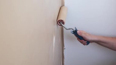 Kadının elini kapayarak beyaz bir duvarı boya rulosuyla bej rengine boyuyor. Ev onarımı, yenileme ve inşaat kavramı