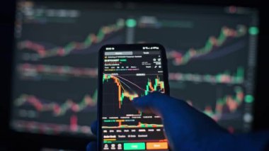 Bir tüccar, pazar verilerini gösteren bir bilgisayar ekranının arkaplanındaki Bitcoin grafiklerini analiz eder. Finans ve yatırım içeriği için ideal.