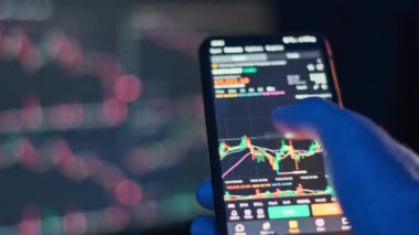 Bir grafik uygulamasındaki kripto döviz piyasası eğilimlerini analiz etmek için akıllı telefon kullanan bir elin yakın çekimi. Finans ve yatırım projeleri için ideal.