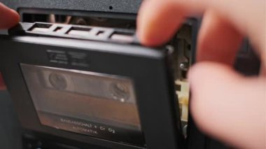 Eller nazikçe bir teybe antika bir kaset yerleştirirken. Dokunsal etkileşimi ve retro mekaniği vurgular. Müzik ya da nostalji temalı projeler için mükemmel.