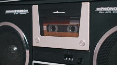 Antika bir teyp kasetinin retro müzik kutusundaki detaylı görüntüleri. Kasete ve makineyle olan etkileşimine odaklan. Nostalji ve müzik projeleri için uygun.