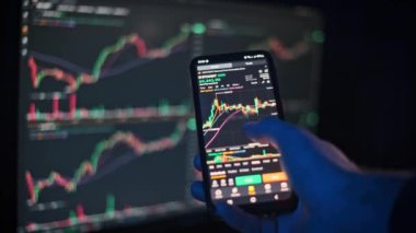 Bir el, kripto para birimi grafiklerini analiz etmek için akıllı telefon kullanıyor. Piyasa verileri, finans, teknoloji ve iş videoları için uygun..