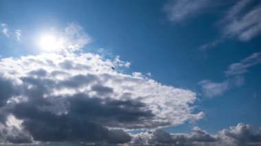 Mavi gökyüzünde ilerleyen tüylü beyaz bulutların zamanı. Güneş soldan parlıyor, bulutları aydınlatıyor ve huzur ve sükunet hissi yaratıyor..