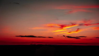 Canlı turuncu ve kırmızı gökyüzüne karşı gölgeli bulutlarla gün batımının büyüleyici bir zamanı. Doğa, zaman ve geçişler ile ilgili projeler için mükemmel..