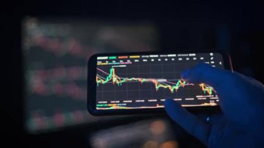 Bir kişi Bitcoin pazar eğilimlerini incelemek için akıllı telefon kullanıyor. Bu klip kripto para, finans ve teknoloji projeleri için uygundur.
