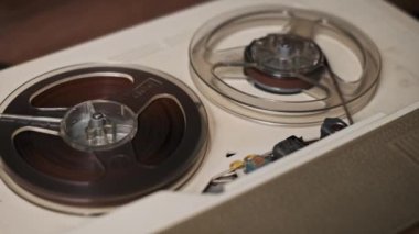 Retro-reel ses kayıt cihazının karmaşık bir yakın çekimi, dönen kaset makaralarını ve detaylı mühendisliği gösteriyor. Analog ses ekipmanlarının nostaljisini yakalar.