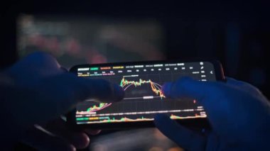 Eller, pazar verilerini gösteren bulanık bir ekran karşısında akıllı telefondaki kripto para çizelgelerinde gezinir ve finans projeleri için dinamik bir görsel yaratır..