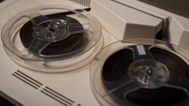Dönen manyetik bantlı iki makaralı bir teybin detaylı yakın çekimi. Analog ses ekipmanlarının çekiciliğini vurgular, klasik müzik temaları veya nostaljik projeler için idealdir.