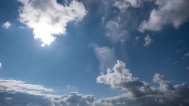 Parlak mavi gökyüzünde ilerleyen beyaz tüylü bulutların zamanı. Güneş çerçevenin ortasında parlıyor, gökyüzünü aydınlatan parlak güneş ışınları yaratıyor..