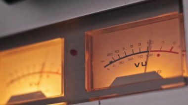 Ses cihazında parlayan eski model bir VU sayacının yakın çekim görüntüsü, sıcak retro estetik ve titiz detaylar sergiliyor. Analog teknoloji ve nostalji temaları için mükemmel..