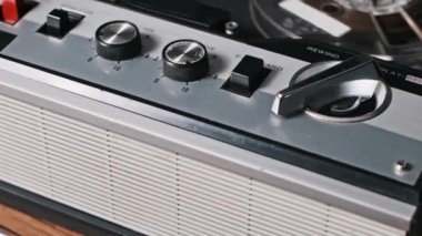 Klasik bir makaradan makaraya kaset kaydedicinin açılı çekimi, dizayn ve kontrollerini gösteriyor, eski moda bir his için sıcak ahşap bir arka plana dayanıyor..