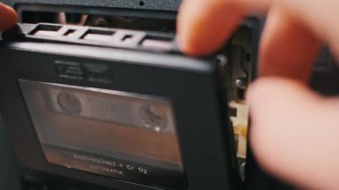 Bir el kullanılmış bir kaseti antika bir teybe yerleştirir. Mekanizma ayrıntılı olarak gösterilir. Geçmişe dönük, nostaljik veya teknolojiyle ilgili projeler için ideal.