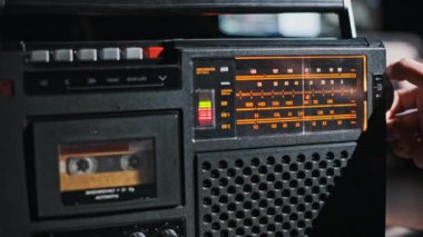 Bir el, sıcak sarı bir arka ışıkla aydınlatılan klasik bir radyo kadranını ayarlar ve retro veya klasik ses projeleri için nostaljik bir sahne yaratır..