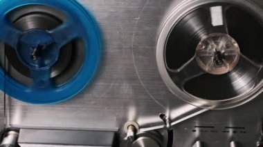 Bir erkek elin, dönen makaraları yakalamak için bobinden bobinine bir kayıt cihazıyla oyun kolunu birbirine bağlamasının detaylı görüntüsü. Antika ses mühendisliğinin analog cazibesini, retro sihrini, manuel işlevini vurgular