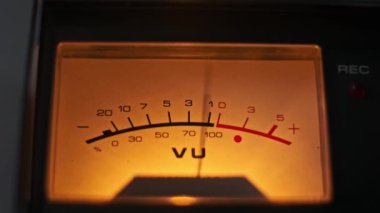 Eski bir VU sayacının yakın plan görüntüsü sıcak bir şekilde parlıyor, retro estetik ve karmaşık analog detaylarını vurguluyor. Nostalji, ses ekipmanları ve müzik üretimi için ideal temalar.