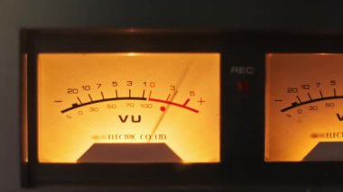 Klasik bir ses cihazının aydınlatmalı bir vintage VU sayacının yakın çekimi, sıcak aydınlatma ve karmaşık tasarım detayları yakalıyor. Analog ses ve retro teknoloji temaları için mükemmel..