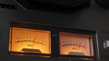 Sıcak kehribar ışığı, retro estetik ve hassas analog kayıt ekipmanlarıyla aydınlatılan klasik bir VU sayacının yakın çekim görüntüsü. Medya ve ses temalı projeler için ideal.