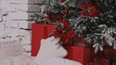 Canlı kırmızı noktalı süslemeler ve süslerle dolu, karla kaplı bir Noel ağacının bulunduğu rahat ve şenlikli bir köşe. Kırmızı ve ekose hediye kutuları aşağıda oturur ve sıcak bir tatil ortamı yaratır..