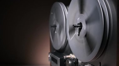 Hareket halindeki dönen makaradan makaraya yakın çekim bir teyp retro tasarımını ve mekanik hassasiyetini vurgular. Loş ışıkta ayarlanmış, nostaljiyi çağrıştırıyor, klasik ses teknolojisinin zamansız cazibesini.
