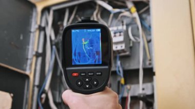 Bir teknisyen, açık bir paneldeki elektrik ve kablo bileşenlerini kontrol etmek için termal görüntüleme kamerası kullanır..