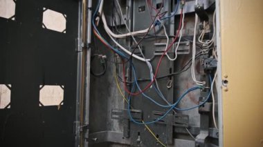 Kısmen maruz bırakılmış metal bir elektrik paneli kutusunun yakın çekimi renkli kabloların karmaşık düzenini gözler önüne seriyor, devre kesicilere bağlanıyor..