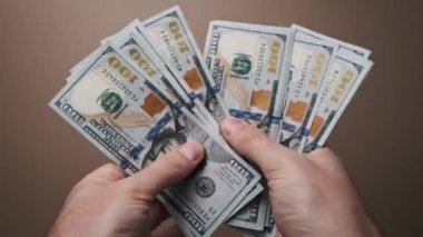 Yakın plan el ele tutuşmalar ve birden fazla 100 dolarlık banknotları tarafsız bir arkaplana karşı yelpazeleme zenginlik işleme, parayı sembolize etme, kazanç.