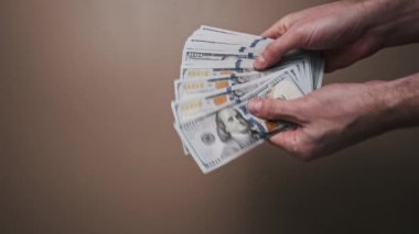 Bir el, 100 dolarlık banknotlardan oluşan büyük bir grubu tutuyor ve el sürüp notları sayıyor. Finans veya ekonomi konuları için mükemmel.