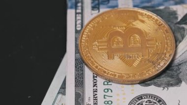 Parlak altın bir Bitcoin madeni para düzgünce istiflenmiş 100 dolarlık banknotların üzerinde duruyor. Dijital ve geleneksel para birimi arasındaki zıtlığı vurgulayan yakın çekim.