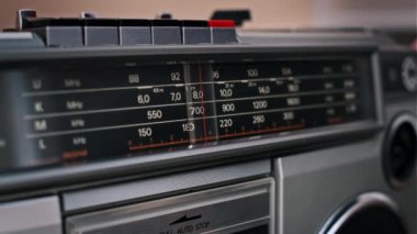 Klasik bir ses sistemindeki istasyonları tarayan iğneye odaklanan radyo arama ekranı. Cihaz retro estetiği ve fonksiyonel tasarımı somutlaştırır..
