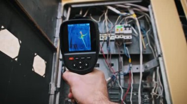 Bir termal kamera, kablo bağlantılarının ve sıcaklıkların net bir görüntüsüyle bir elektrik kutusunun içini inceler. Güvenlik ve teftişle ilgili içerik için ideal.