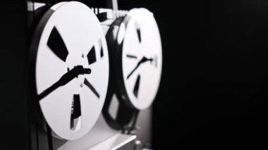 Eski bir makaradan makaraya yakın çekim kasedi, makaraları dönüyor, kaset karanlık bir ortamda sorunsuzca hareket ediyor, dramatik ve nostaljik bir his yaratıyor..